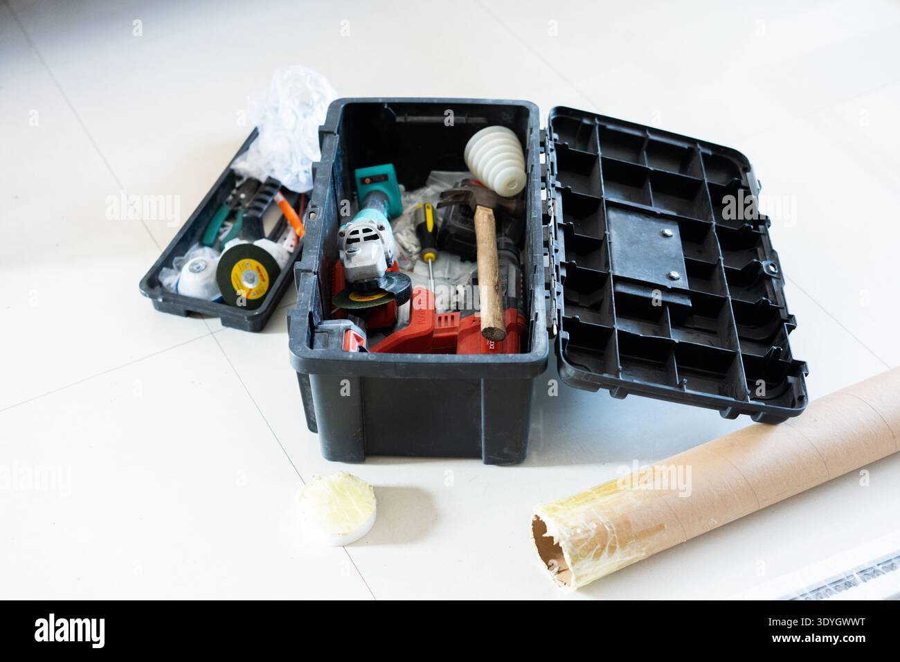 Open black toolbox with power tools and hardware on white floor, construction or DIY project setup Stock Photo