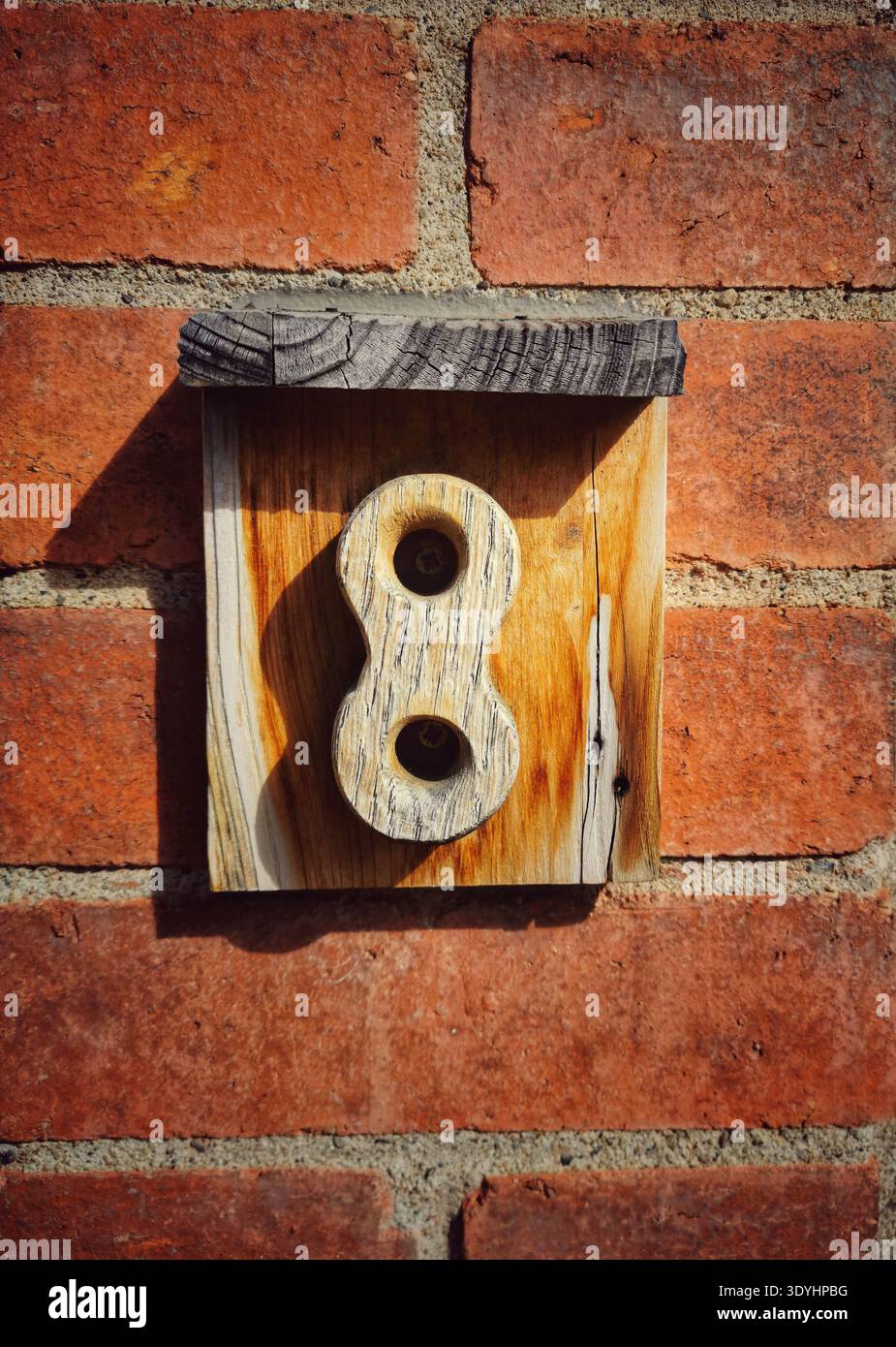A carved wooden number 8 is attached to a smaller wooden plaque mounted on a rough red brick wall. - Smartphone Captured Stock Image