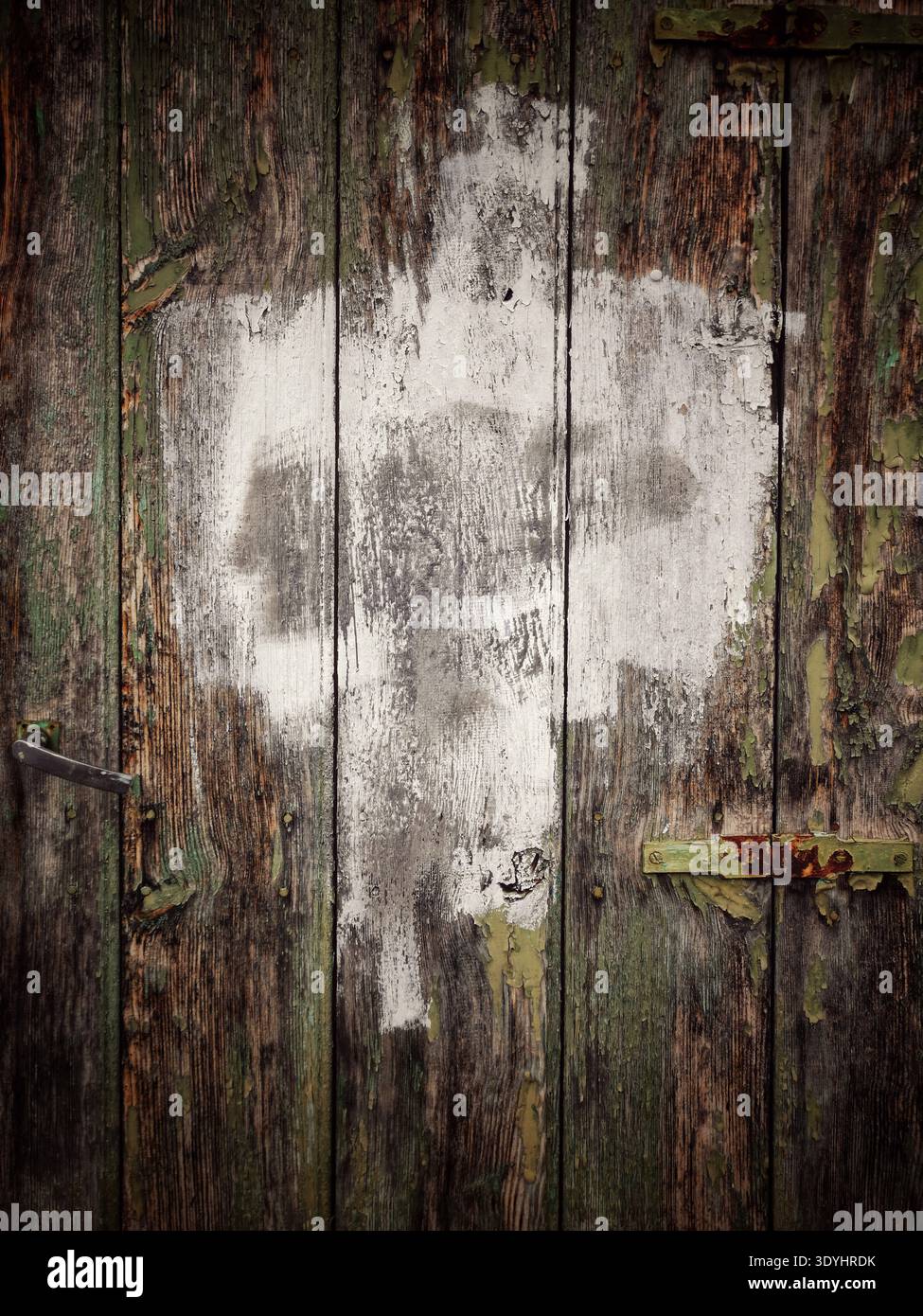 Close up on an aged wooden door. Some green paint shows beneath the worn wood. The door features a handle, hinges, and a section of faded white paint - Smartphone Captured Stock Image