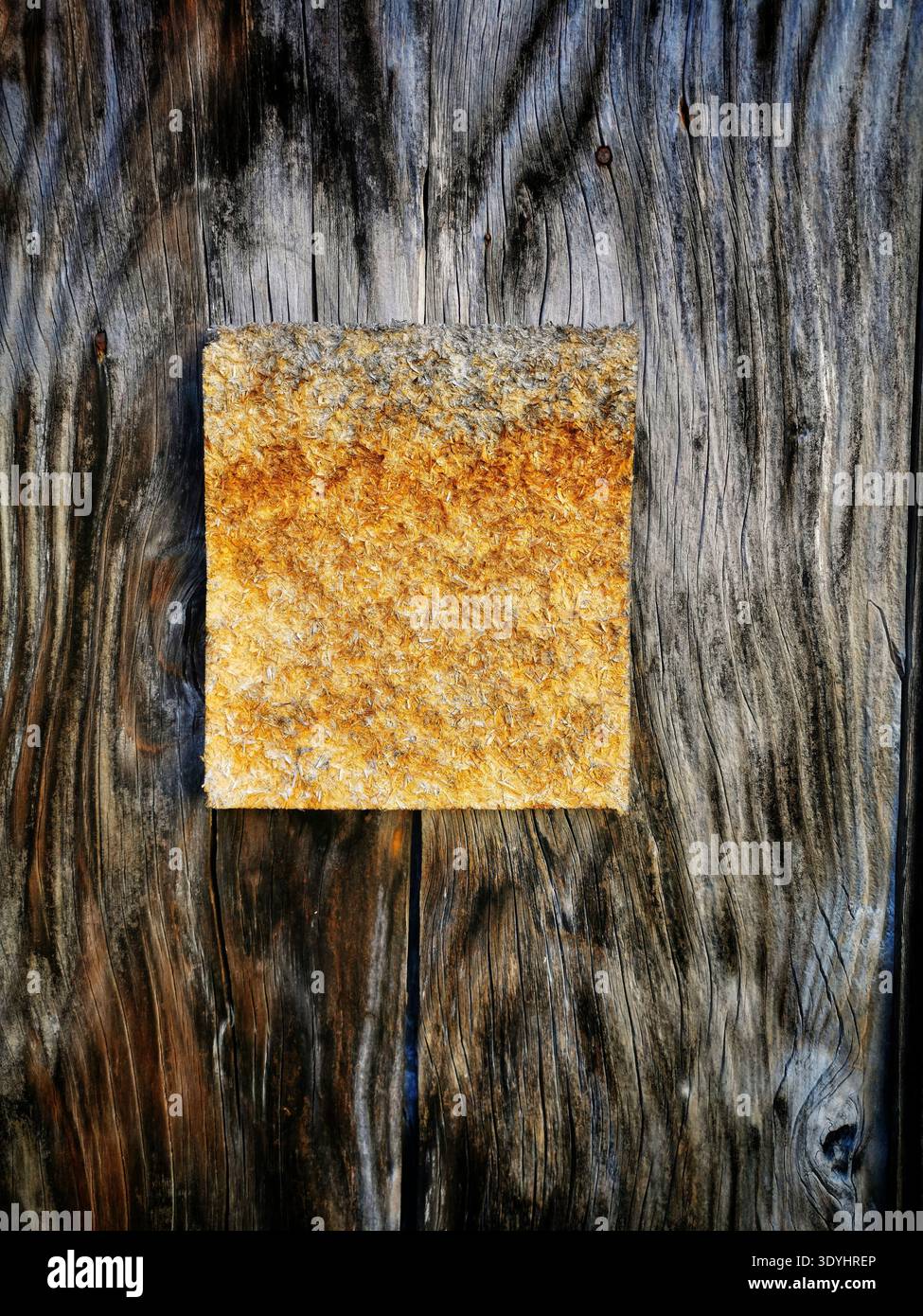 A square, rough textured material, changing from grey to golden-orange, is secured by two screws onto a surface of dark, - Smartphone Captured Stock Image