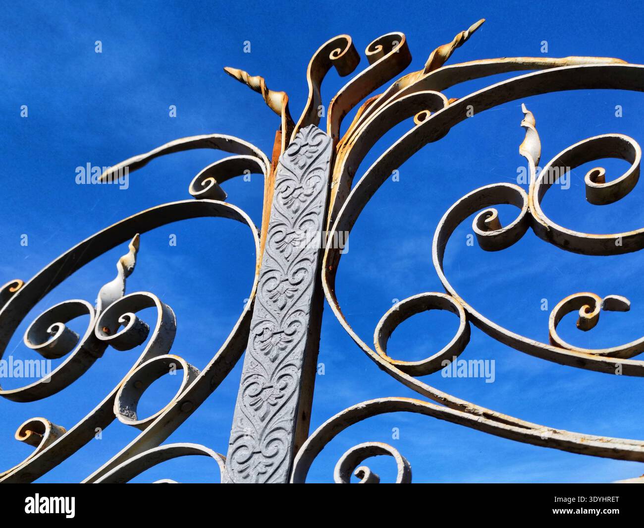 Close-up view of an aged metal gate displaying elegant scrollwork and a central pillar adorned with delicate carved designs. - Smartphone Captured Stock Image