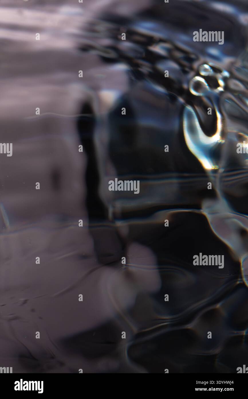 308.Close-up of water surface showing abstract ripples, refractions, and reflections. Glossy and matte areas blend with light distortions, creating fl Stock Photo