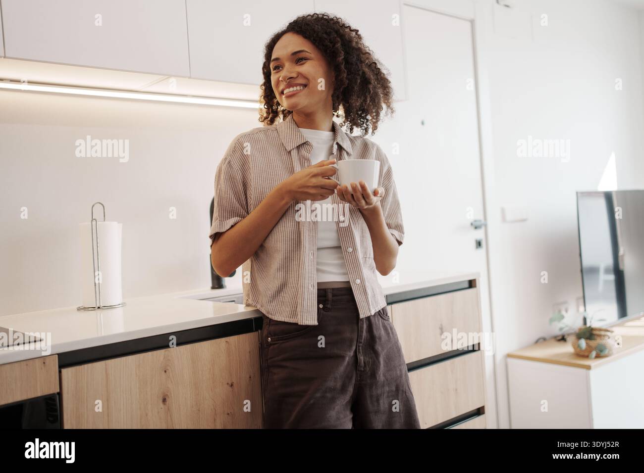 Female Expressing Happiness While Holding Mug In Comfortable Kitchen Environment With Bright Sunlight Stock Photo