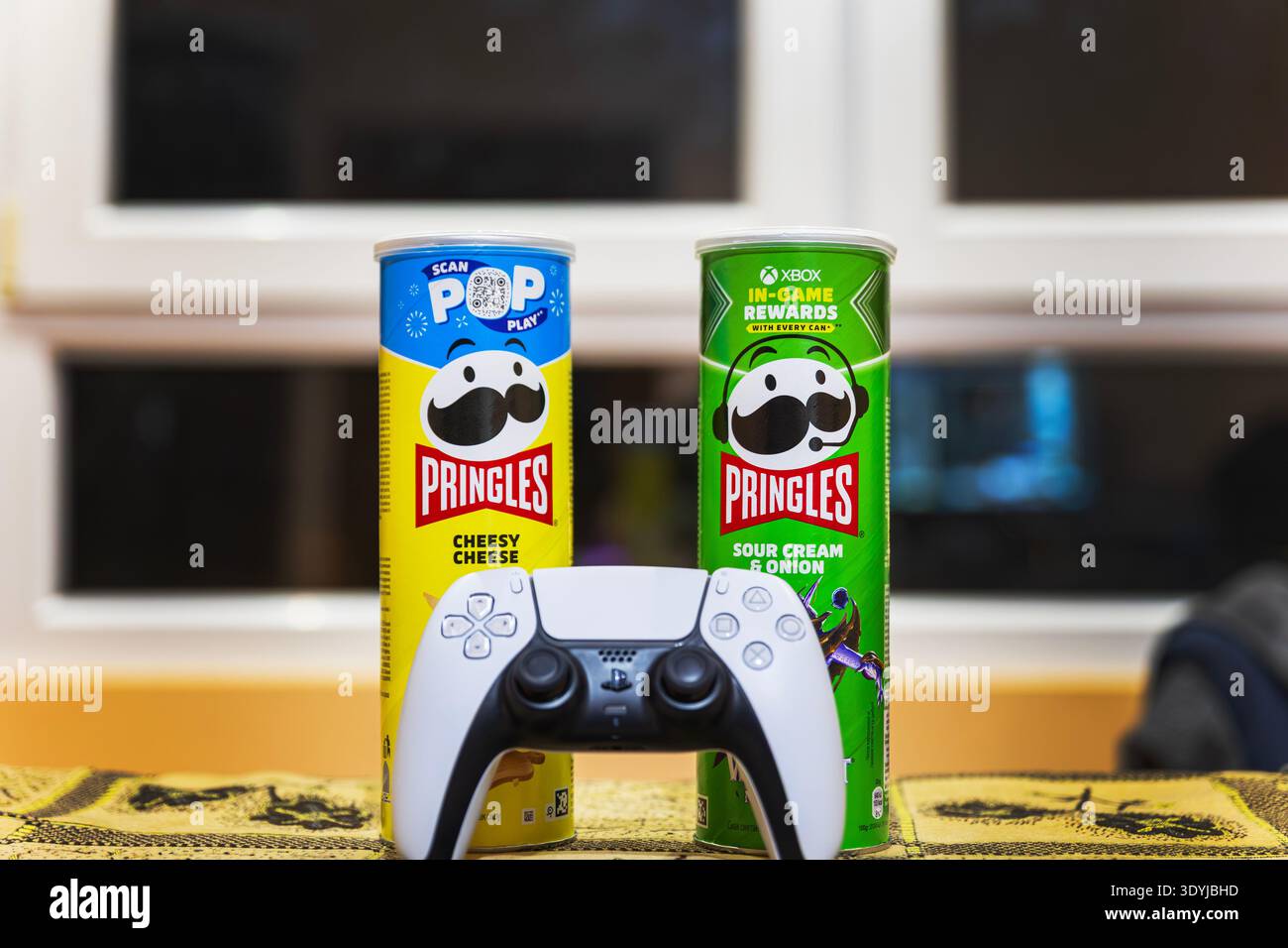 White gaming console controller on a table with potato chips cans. Stock Photo