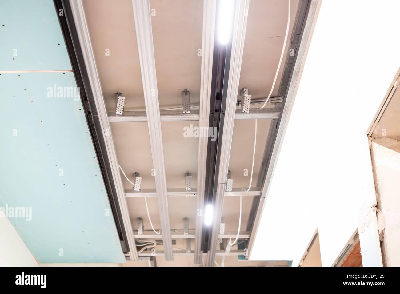 Modern suspended ceiling installation featuring illuminated track lighting with visible metal framework and integrated LED lights in a construction se Stock Photo