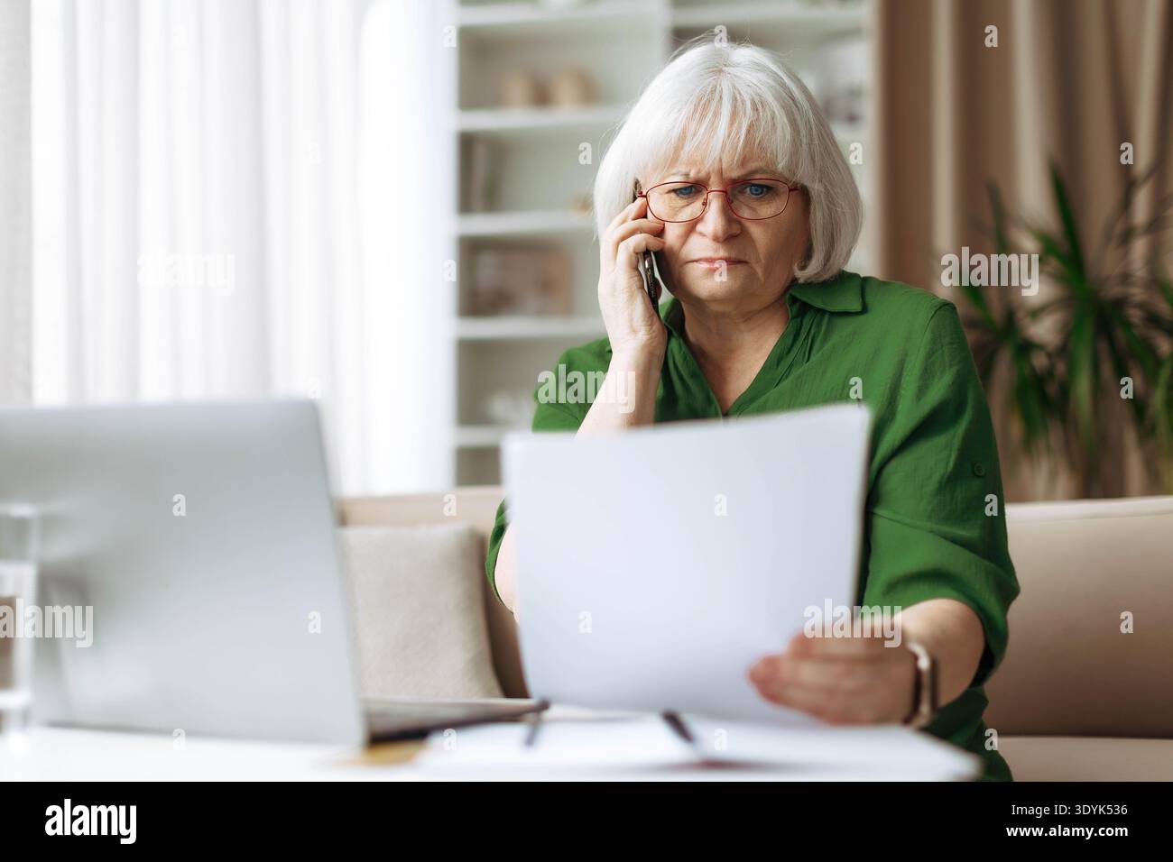 Senior woman talking on phone while checking documents at home Stock Photo