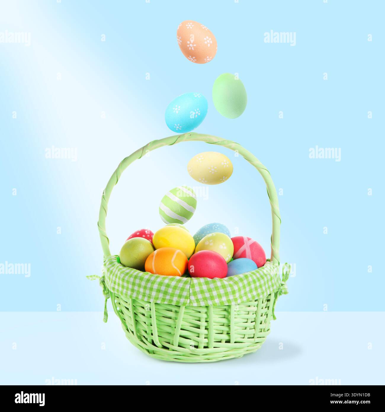 Color Easter eggs falling into basket on light blue gradient background Stock Photo