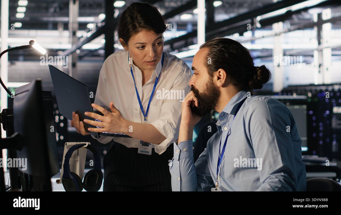 Data center admins working together, collaborating on neural network software development. Teamworking server hub colleagues implementing artificial intelligence technology in workplace, camera A Stock Photo