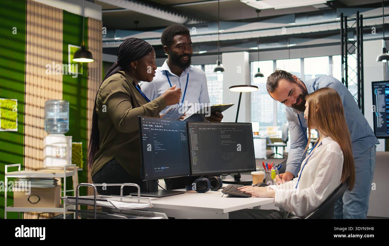 Friendly coworkers helping junior dev code AI algorithms to debug software issues and improve systems, teamwork concept. Welcoming team assisting newcomer in tech startup office, camera A Stock Photo