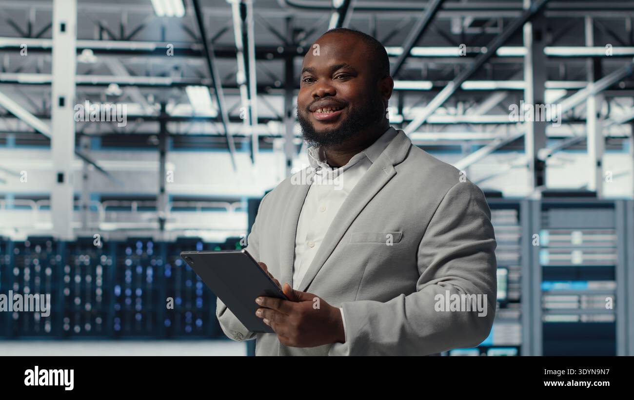Engineer working in server farm using tablet to analyze data. IT professional examining infrastructure in data center using device, ensuring system integrity and security, camera B Stock Photo