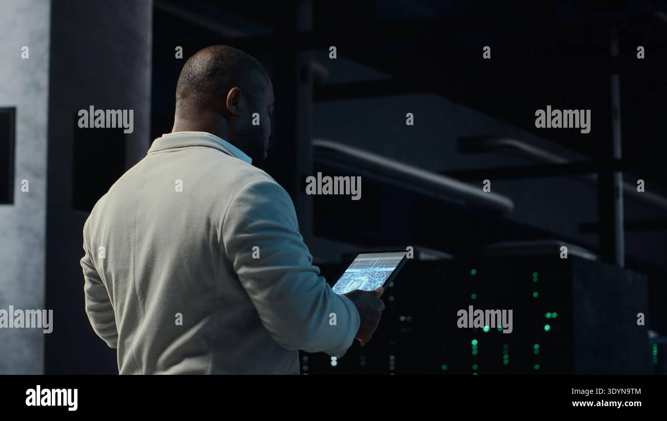 Software developer in data center using tablet, employing AI machine learning models. Employee using device to fulfill artificial intelligence infrastructure needs, allocating resources, camera B Stock Photo