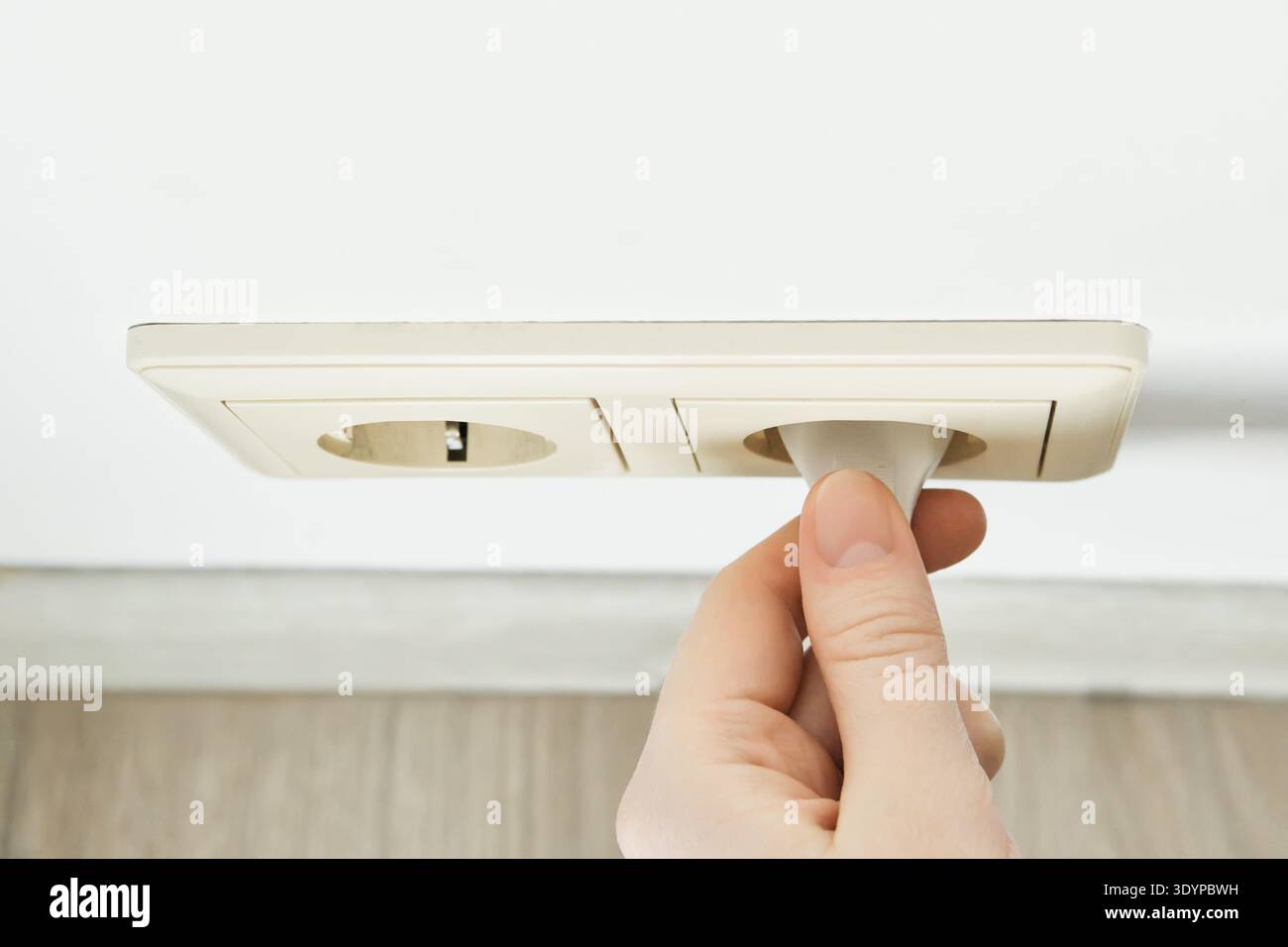 Hand inserting an electric plug into an electrical outlet for energy Stock Photo