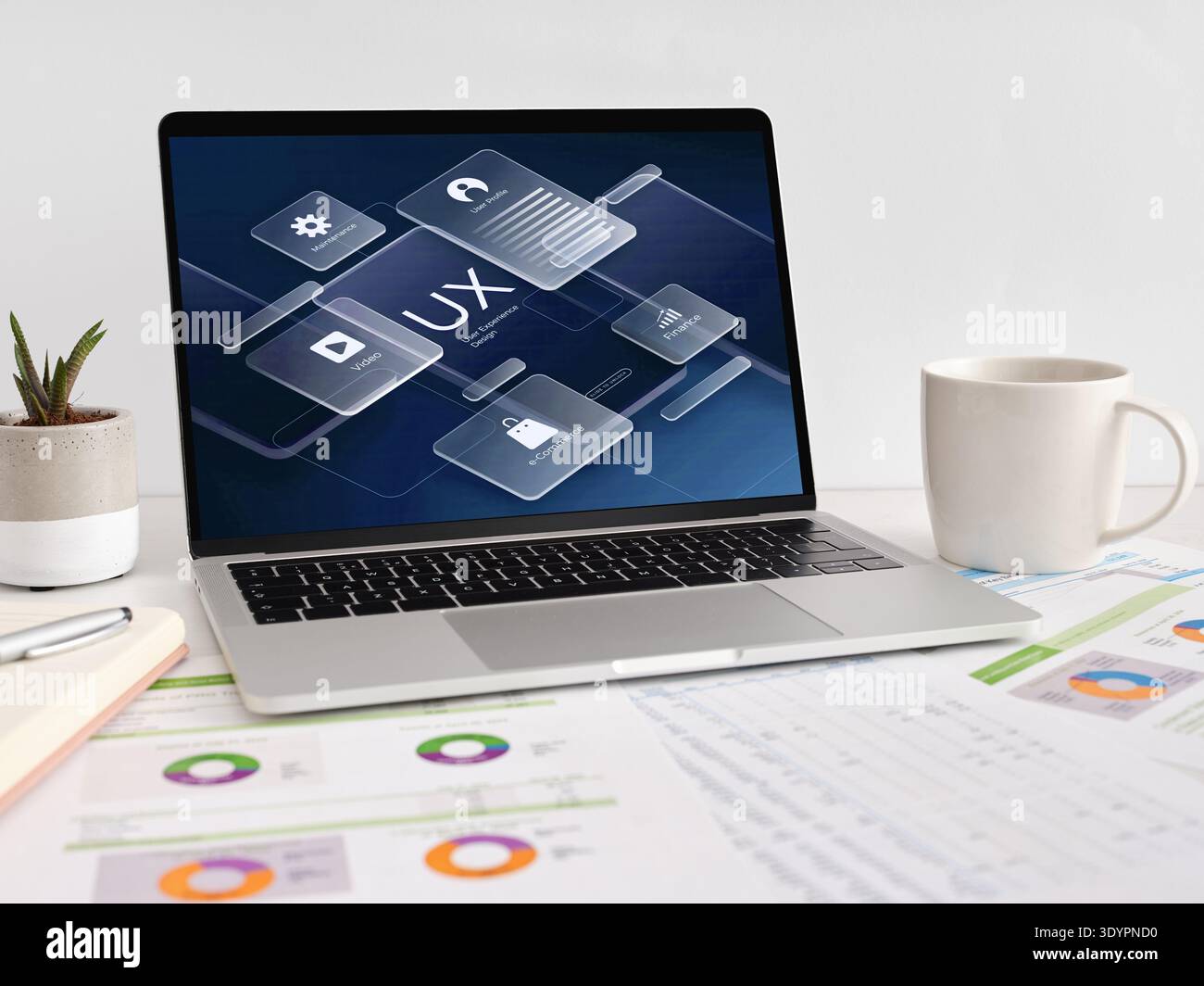 Laptop showing UX design, user interface, and digital marketing concepts. Coffee cup, plant, and financial charts on desk Stock Photo