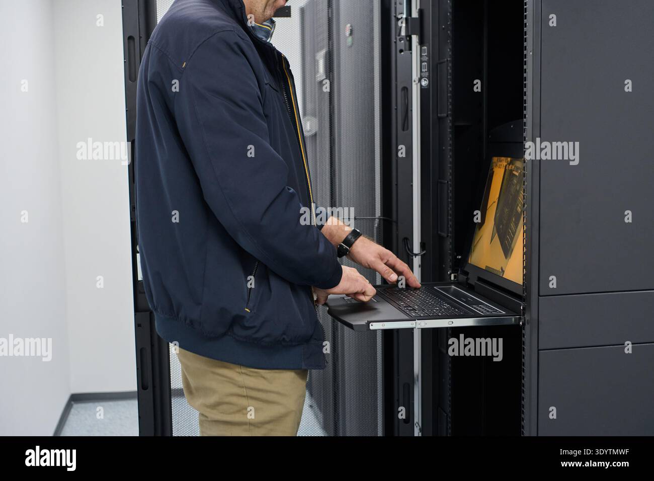 IT technician working on rack-mounted servers using a pull-out laptop console in a data center Stock Photo