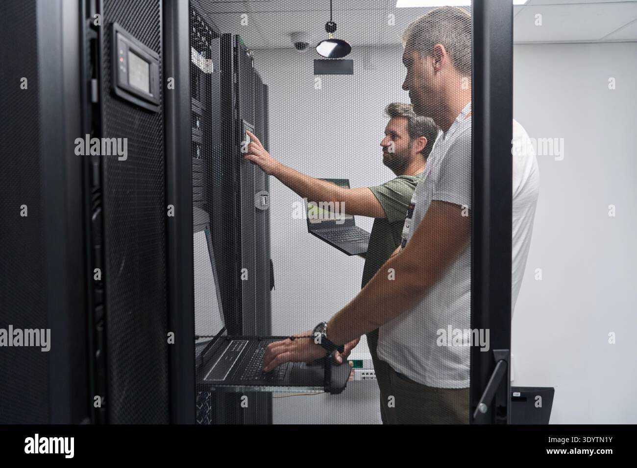 Two IT technicians troubleshooting servers in a secure data center server room with laptops Stock Photo