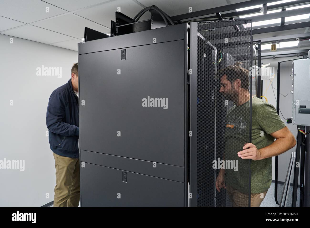 Two technicians installing and inspecting servers in a modern data center rack room for network infrastructure Stock Photo