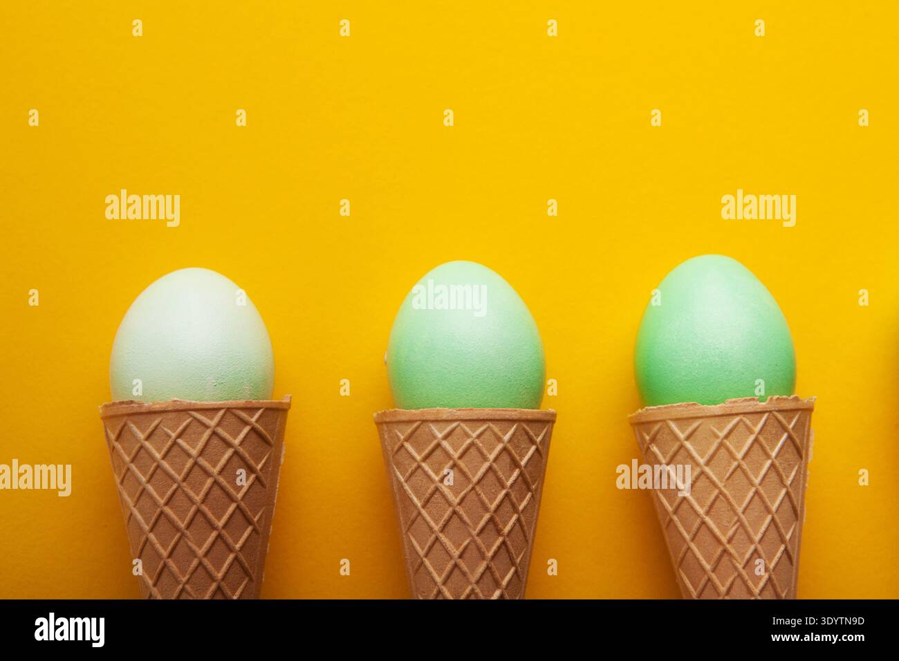 Green easter eggs in waffle cones on yellow background Stock Photo