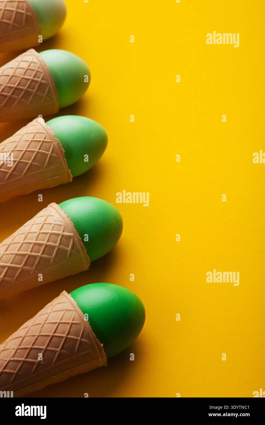 Green easter eggs in waffle cones on yellow background Stock Photo
