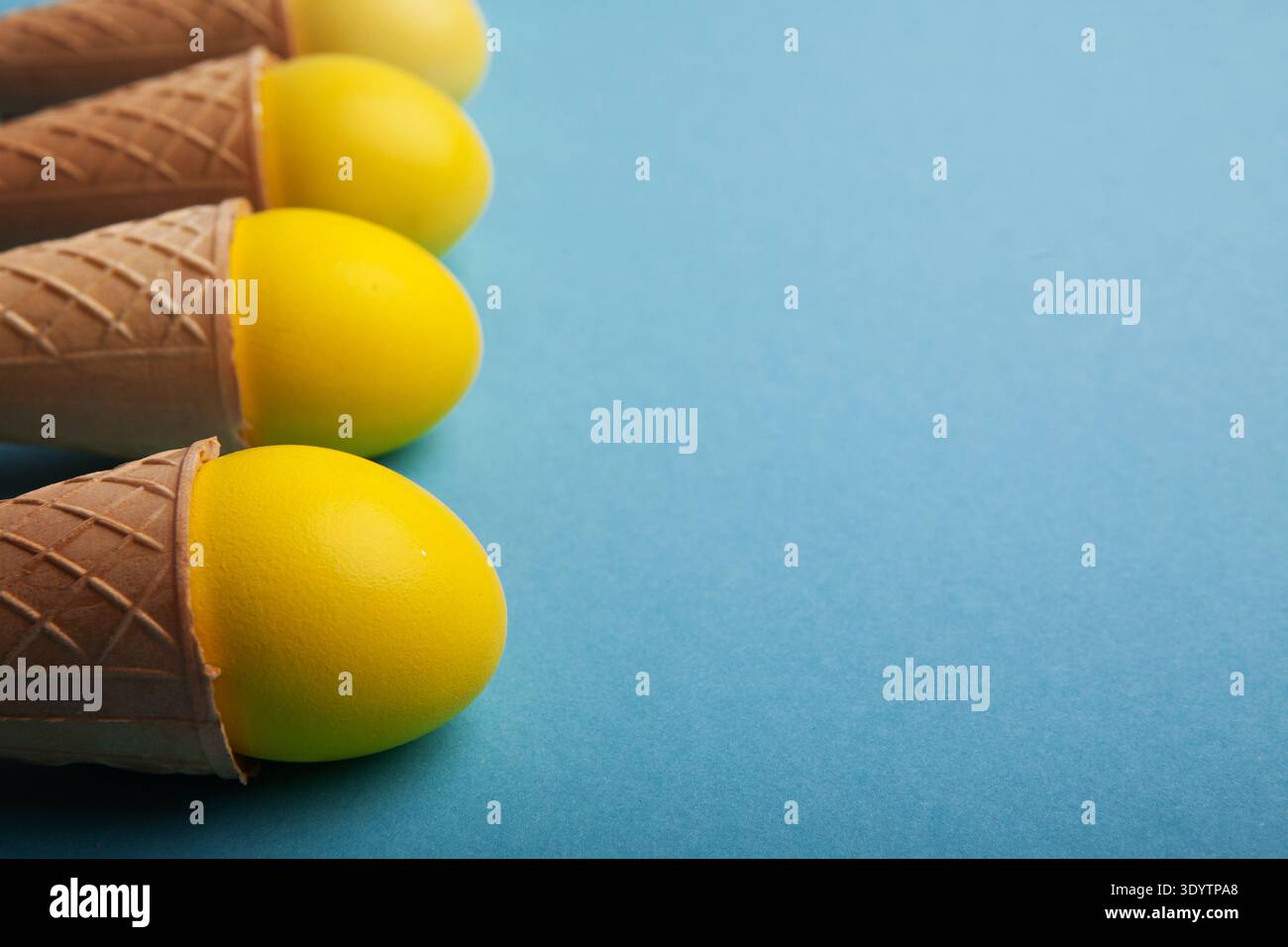 Yellow easter eggs in waffle cones on blue background Stock Photo