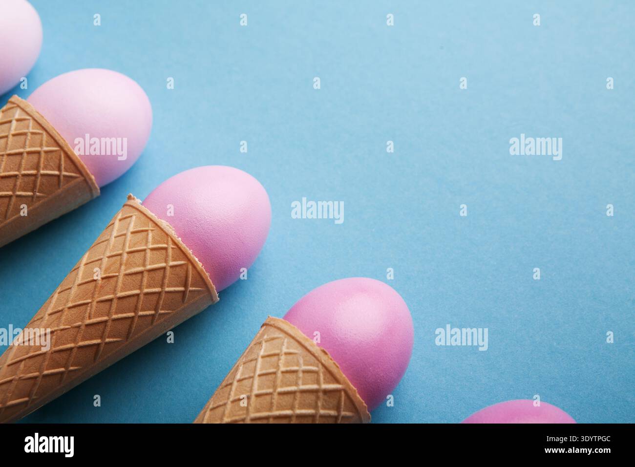 Pink easter eggs in waffle cones on blue background Stock Photo
