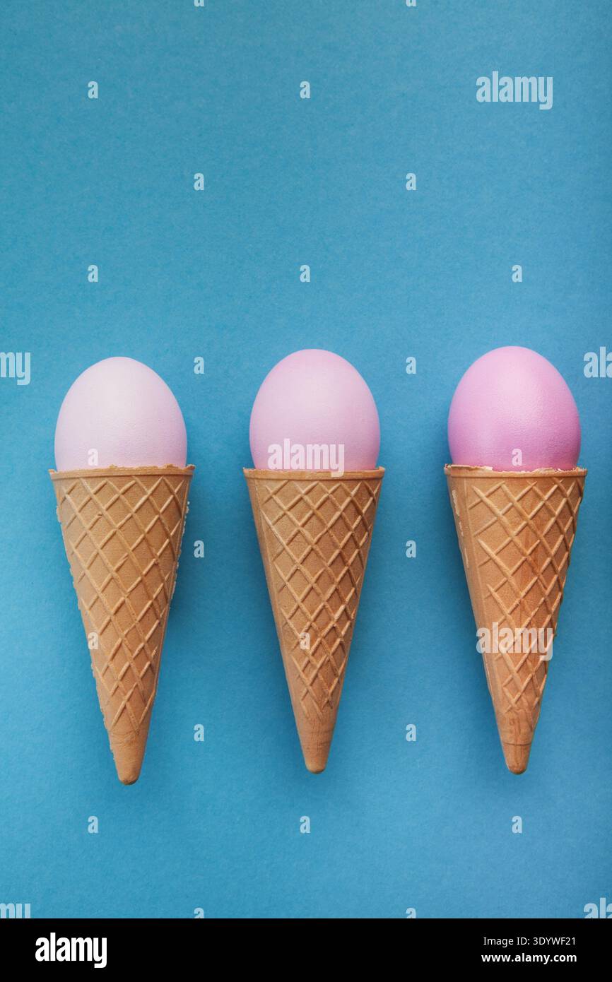 Pink easter eggs in waffle cones on blue background Stock Photo