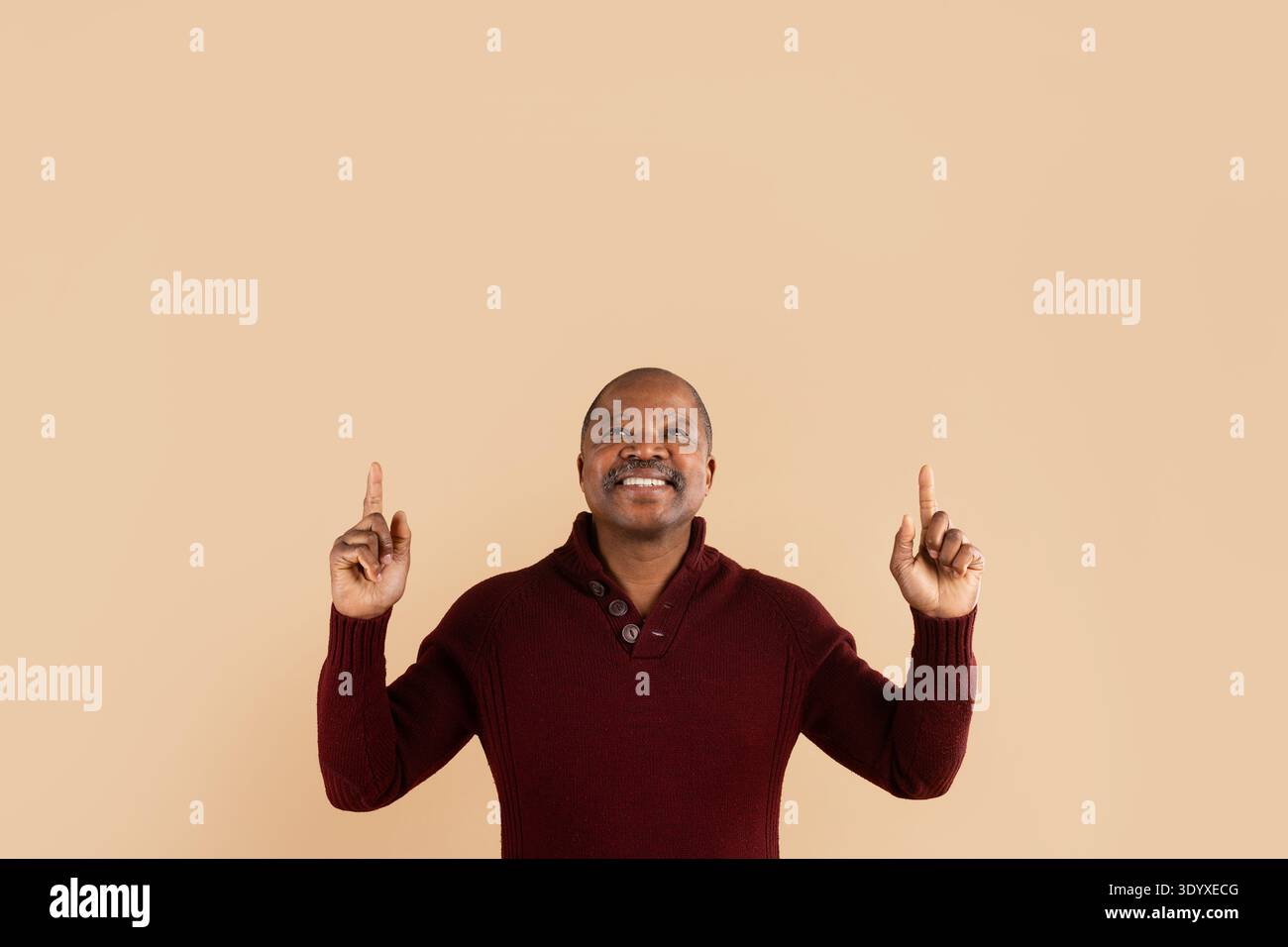 Black man pointing upward with hand gesture while smiling on beige background Stock Photo