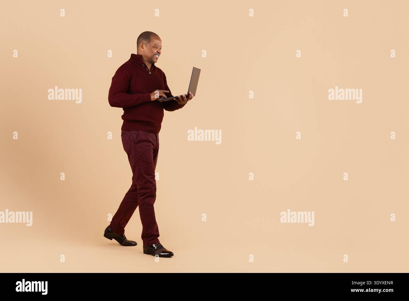 Mature black man walking while using laptop on beige studio background Stock Photo
