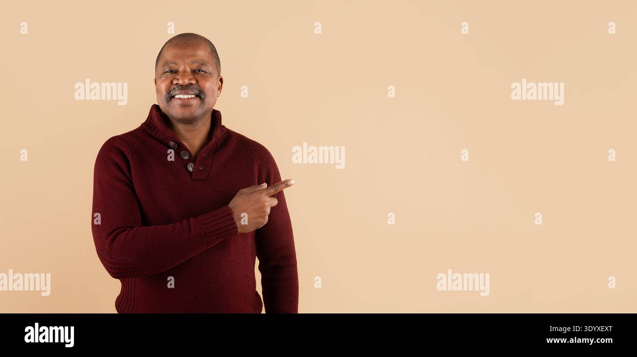 Smiling black man pointing aside with hand while posing on beige background Stock Photo