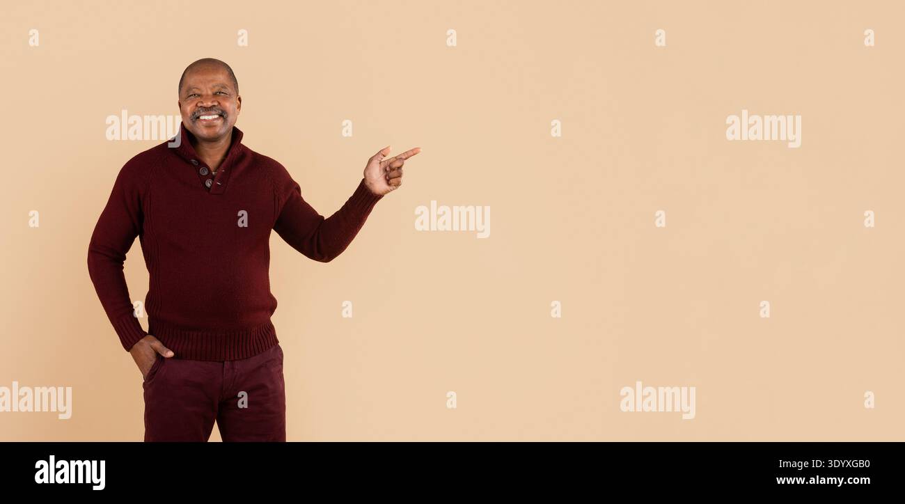Black man in sweater pointing to aside with hand on beige background Stock Photo