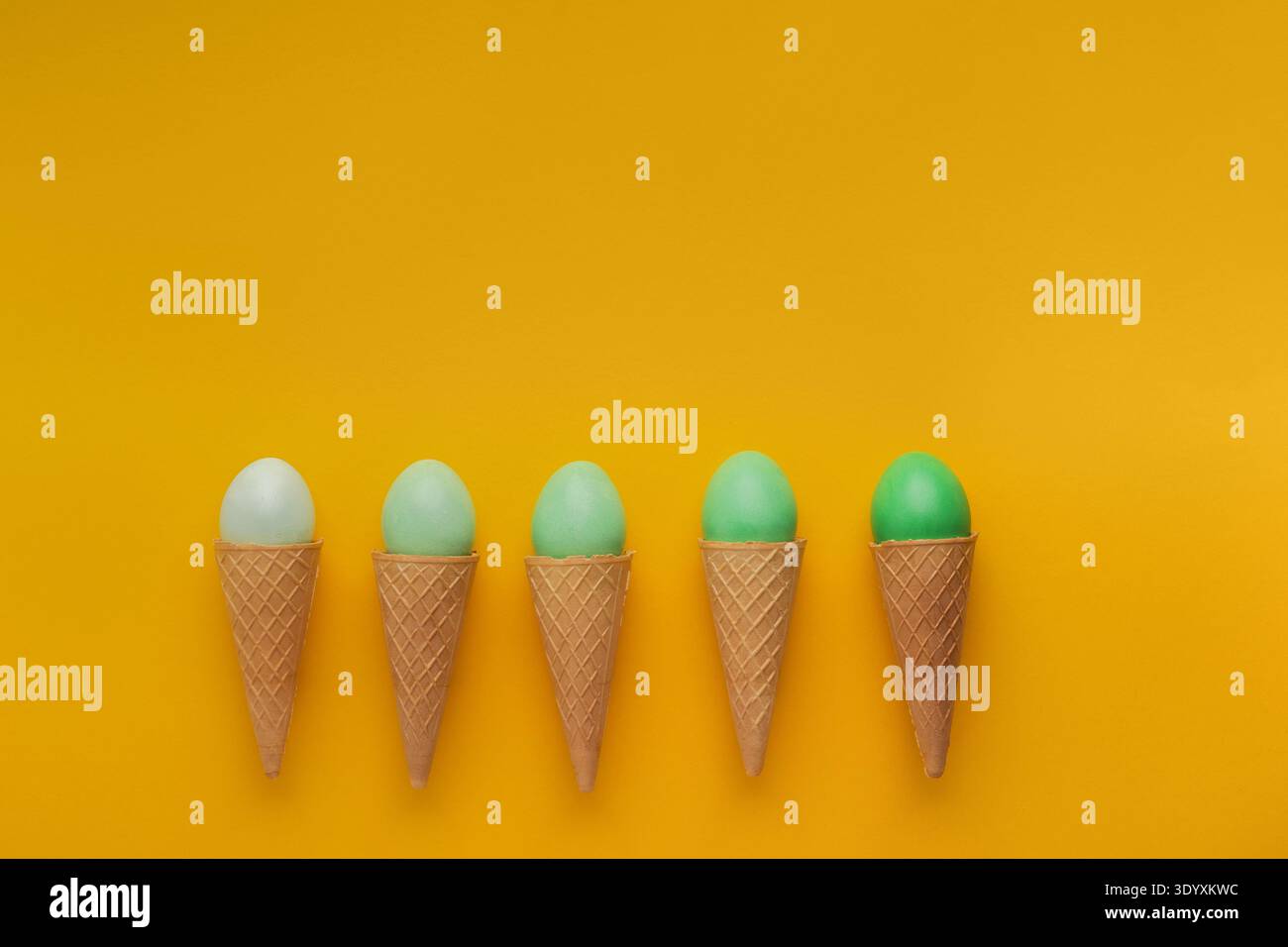 Green easter eggs in waffle cones on yellow background Stock Photo