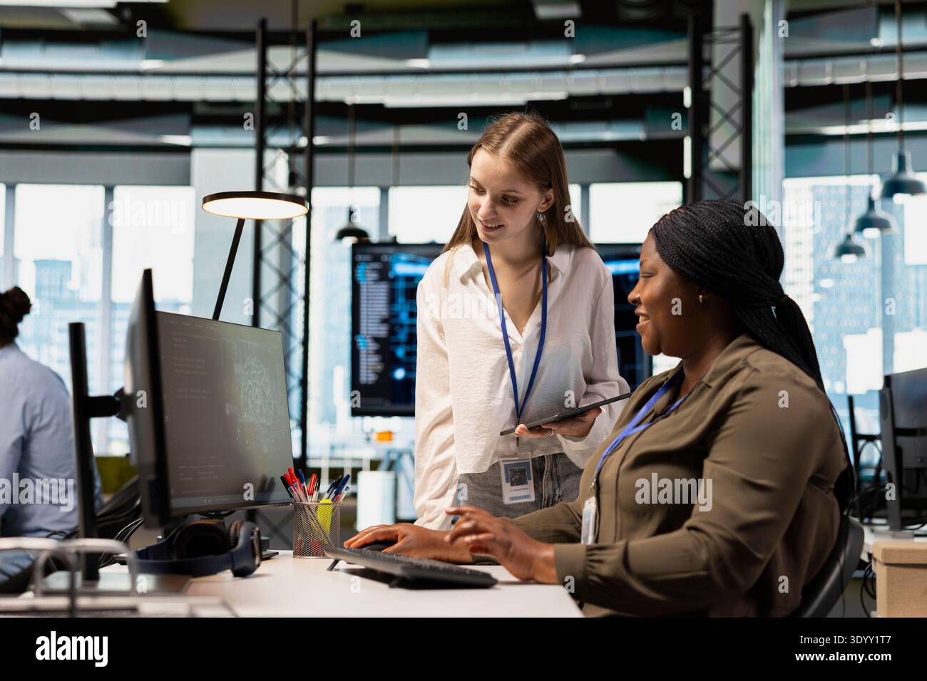 Friendly IT expert teaching intern to use artificial intelligence. Jolly manager guiding junior dev through AI tool integration, mentoring her on using machine learning APIs Stock Photo