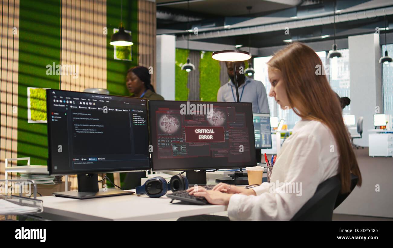 Female engineer in startup office struggling to fix critical error warning popup. Intern doing maintenance on computer glitches while coding in software development agency, camera A Stock Photo