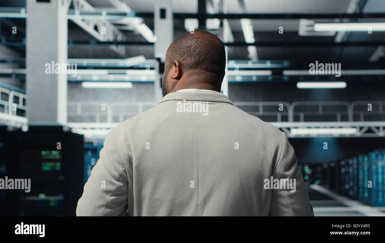 Admin walking in high tech data center facility, checking equipment for system stability. IT specialist overseeing server room, configuring supercomputers, optimizing performance, camera B Stock Photo