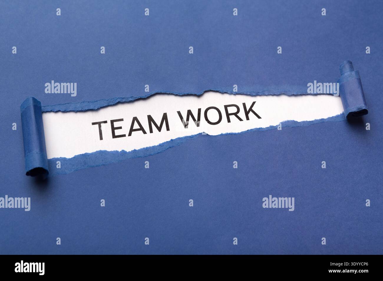Text Team work on white background appearing behind torn blue paper Stock Photo
