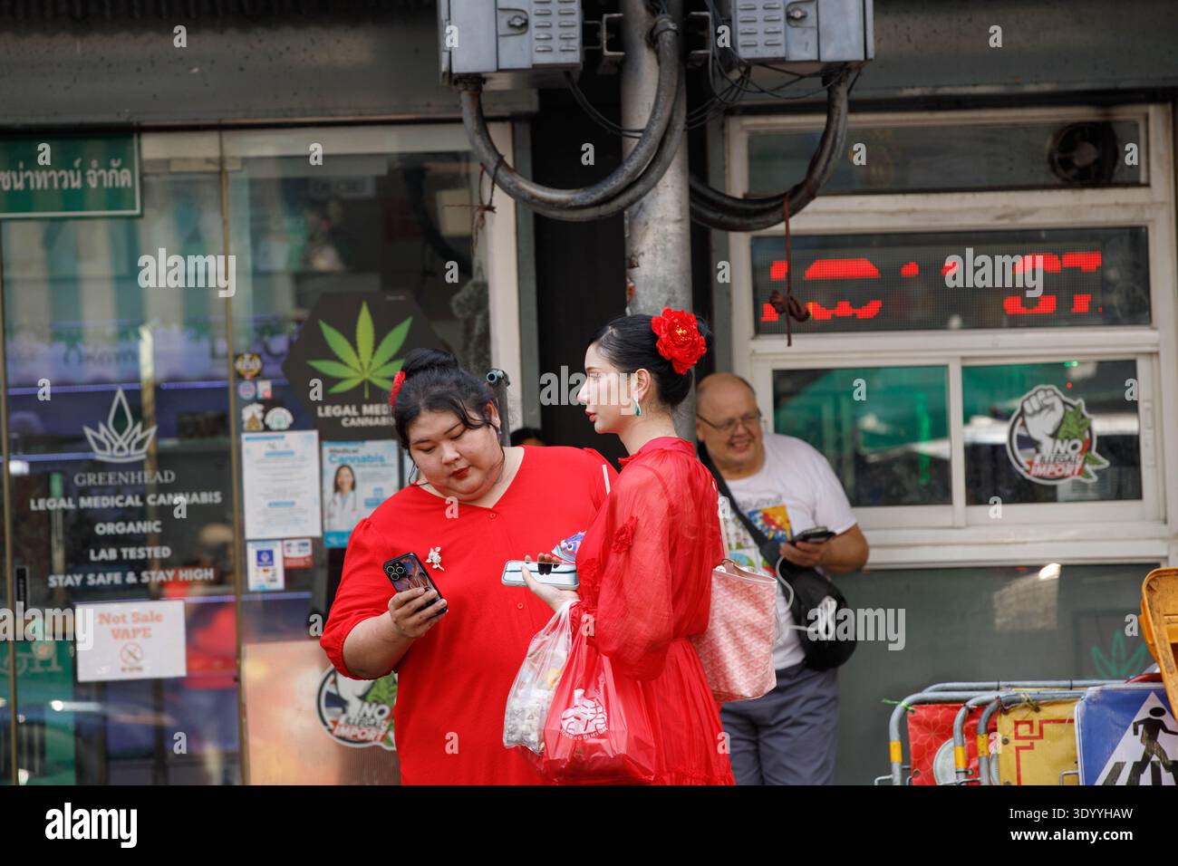BANGKOK, THAILAND-FEB 15, 2026: Two women in red dresses shopping in market, Thai weekend market lifestyle, wide view, at Yaowarat. Stock Photo