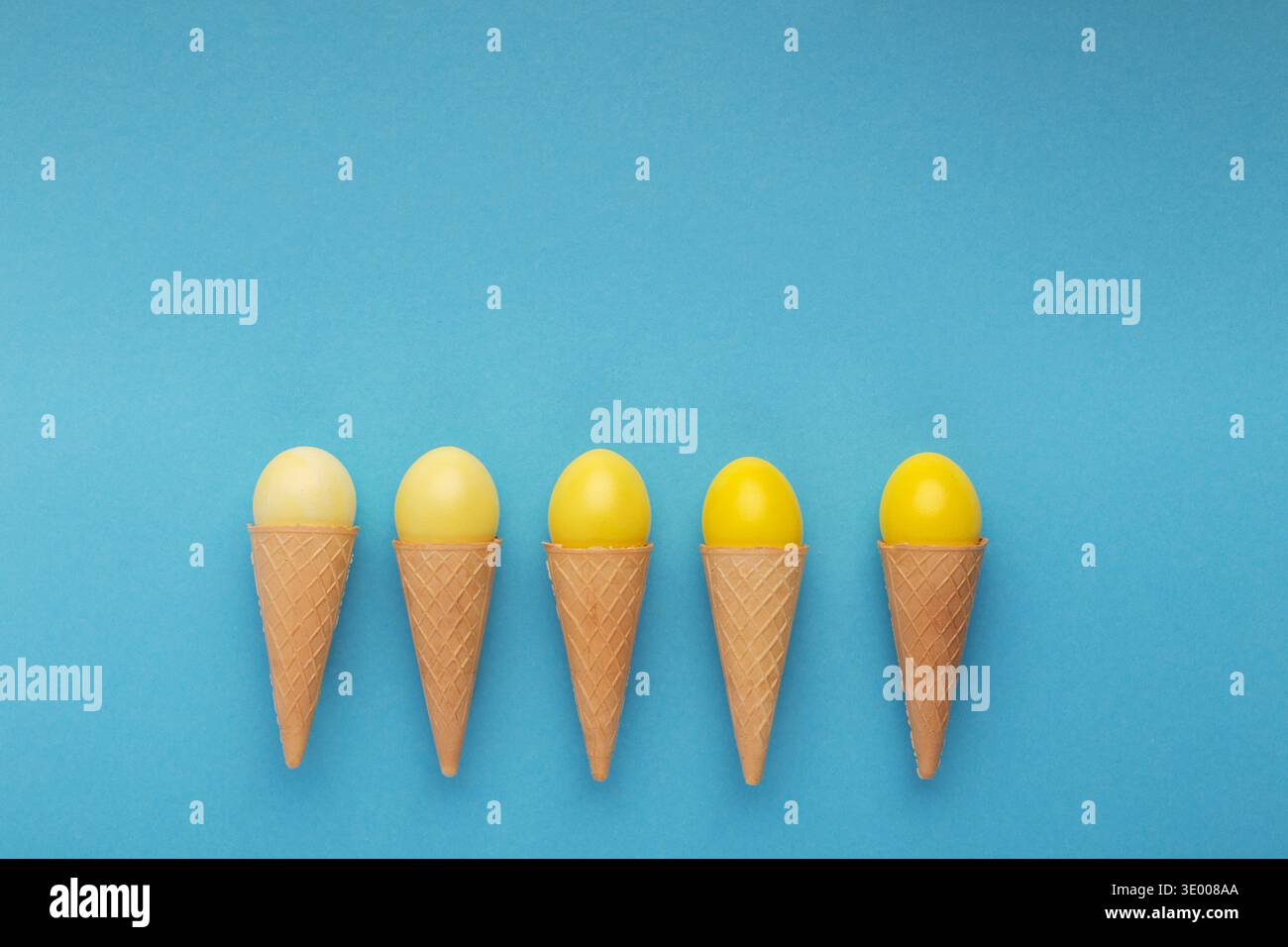 Yellow easter eggs in waffle cones on blue background Stock Photo