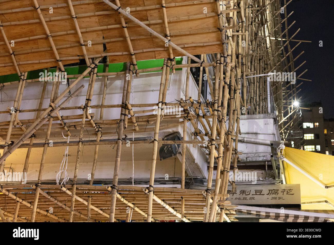 Traditional bamboo scaffolding erected around a building under renovation at night on Tung Choi Street in Mong Kok, Kowloon, Hong Kong. Stock Photo
