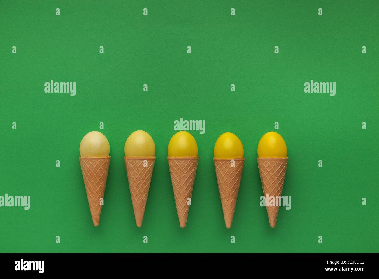 Yellow easter eggs in waffle cones on green background Stock Photo