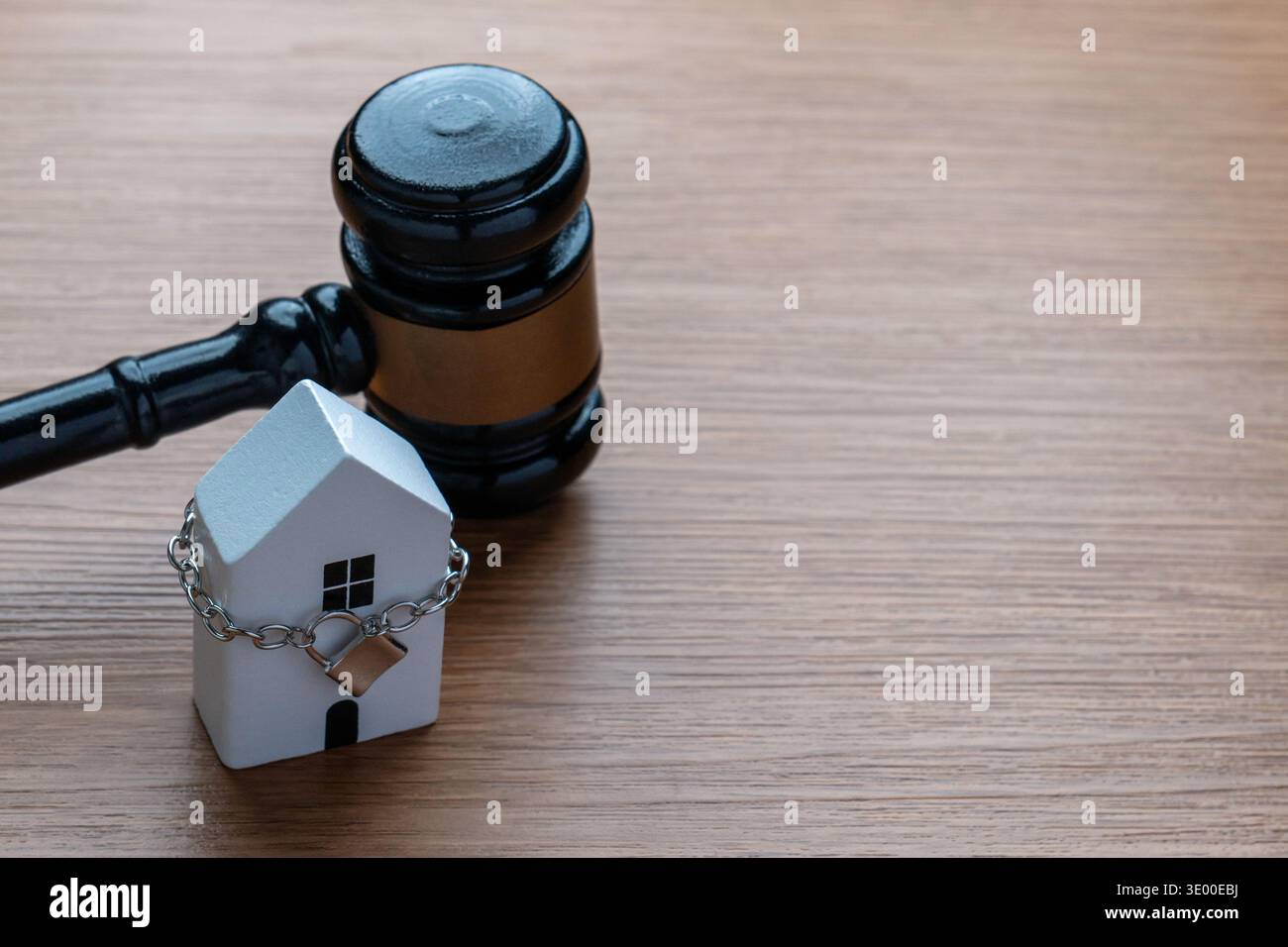 A miniature house wrapped in a silver chain with a padlock next to a gavel. Foreclosure, property law, eviction, real estate disputes Stock Photo