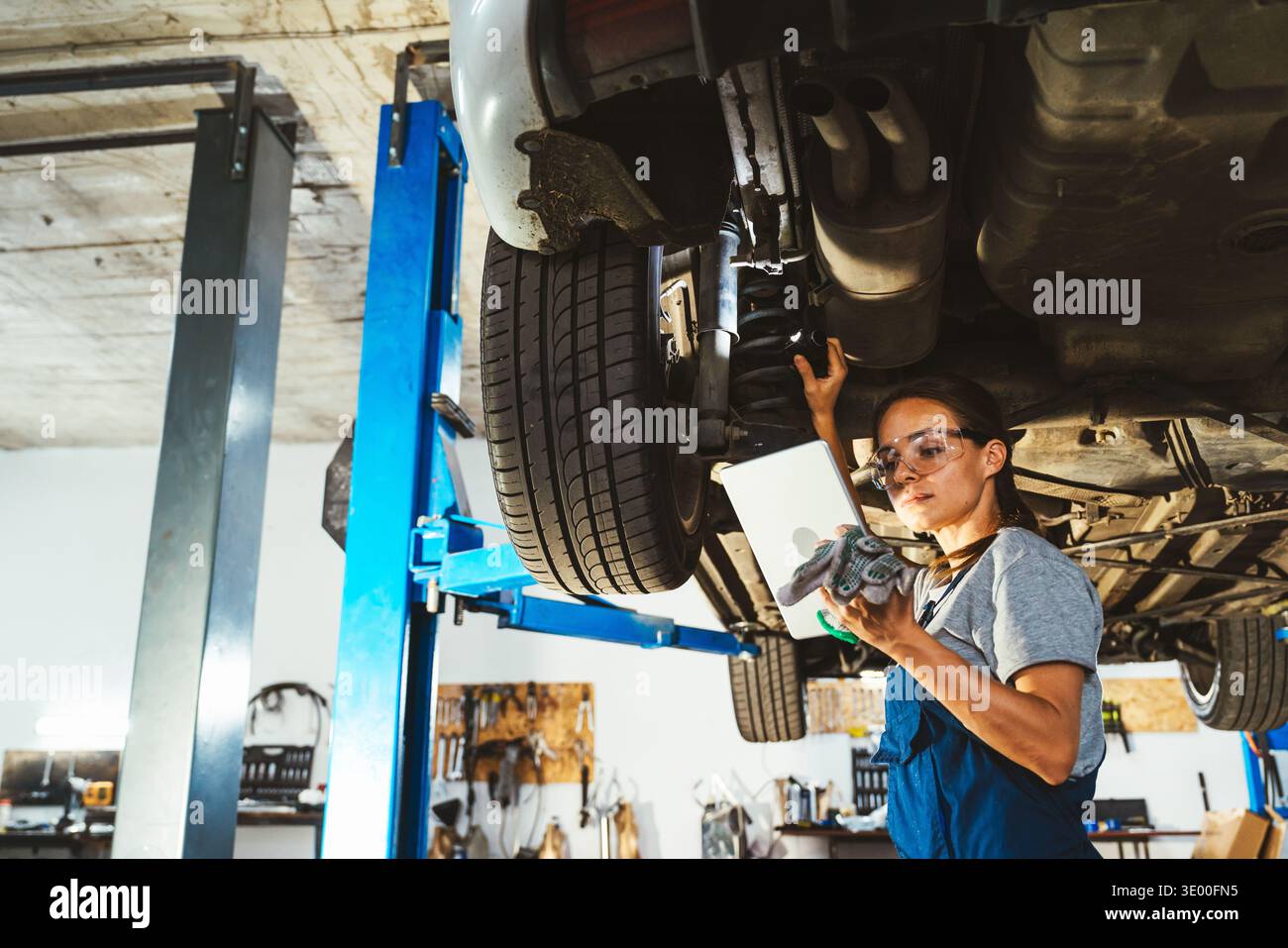 Professional female mechanic inspecting car in auto repair shop using digital tablet Stock Photo