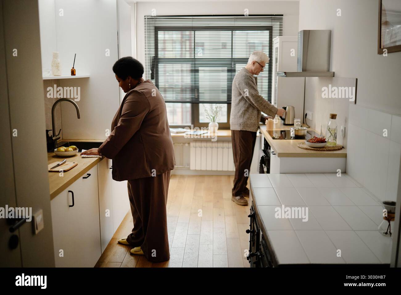 Senior Caucasian Man and Senior Black Woman Preparing Food in Modern Kitchen Stock Photo