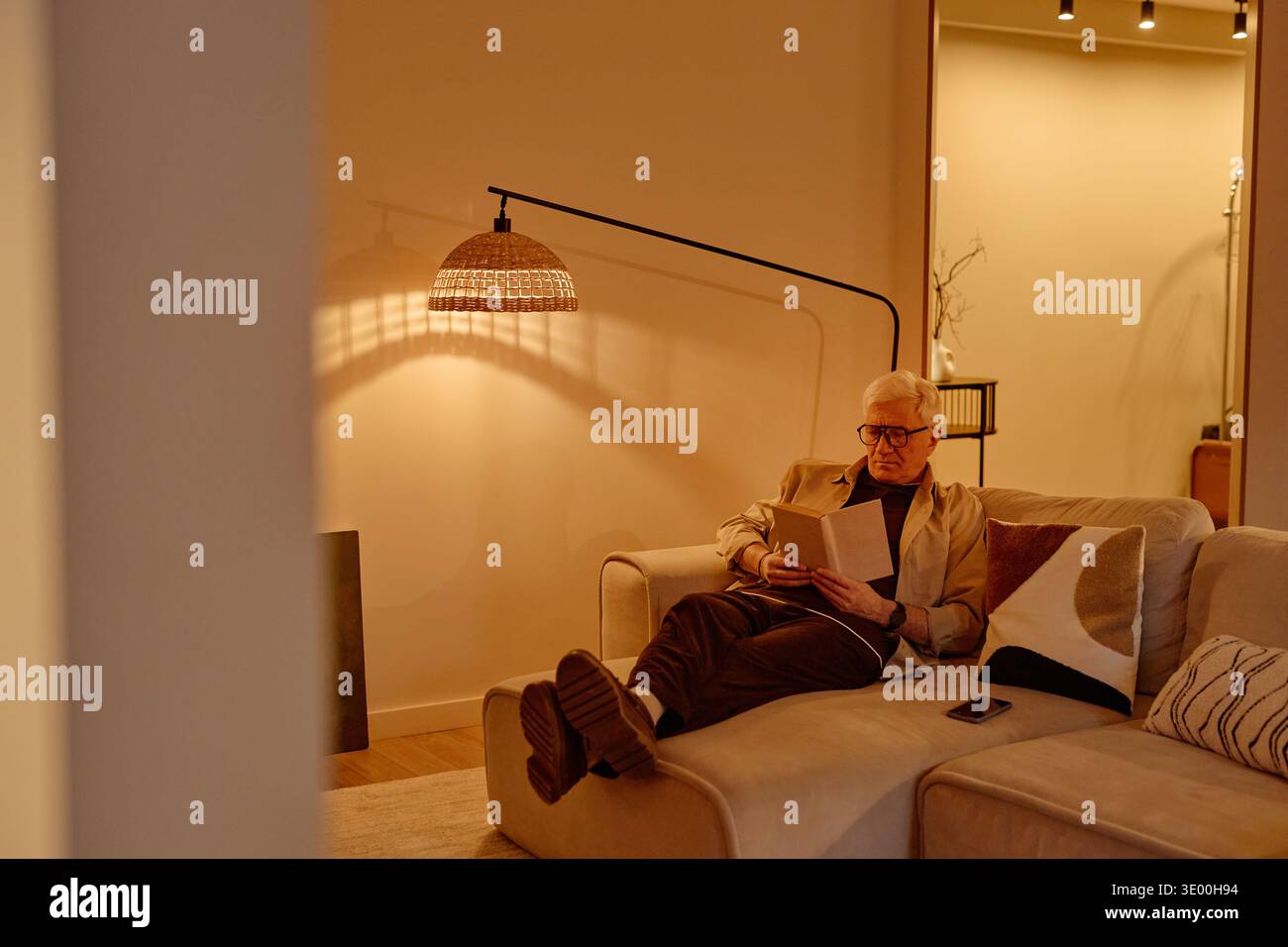 Senior Caucasian Man Sitting on Sofa Reading Book in Cozy Living Room Stock Photo