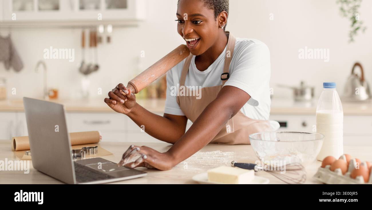 Woman Using Laptop While Baking in Kitchen During Daytime With Various Ingredients on Table Stock Photo