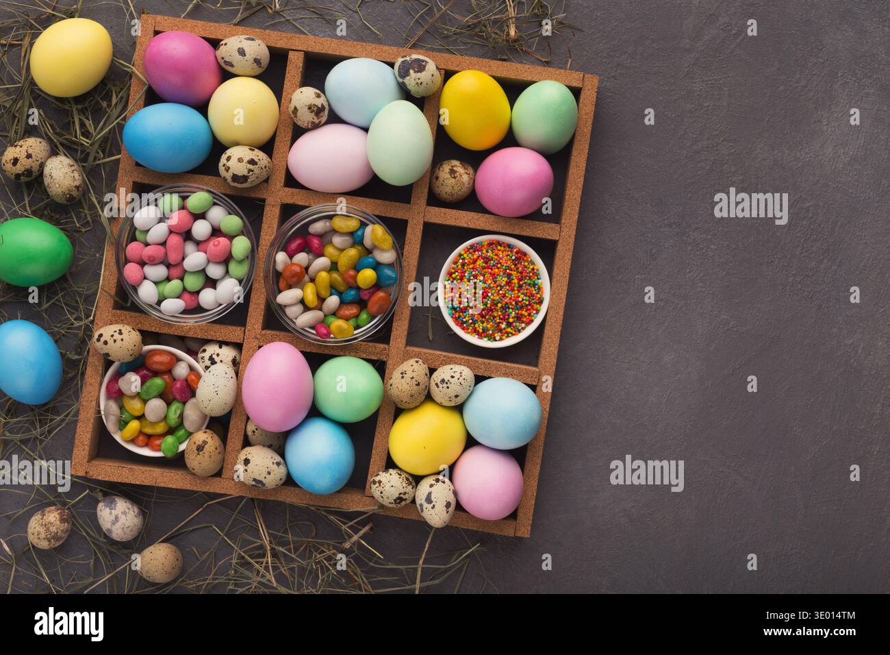 Colored easter eggs and small candies in frame on gray background Stock Photo