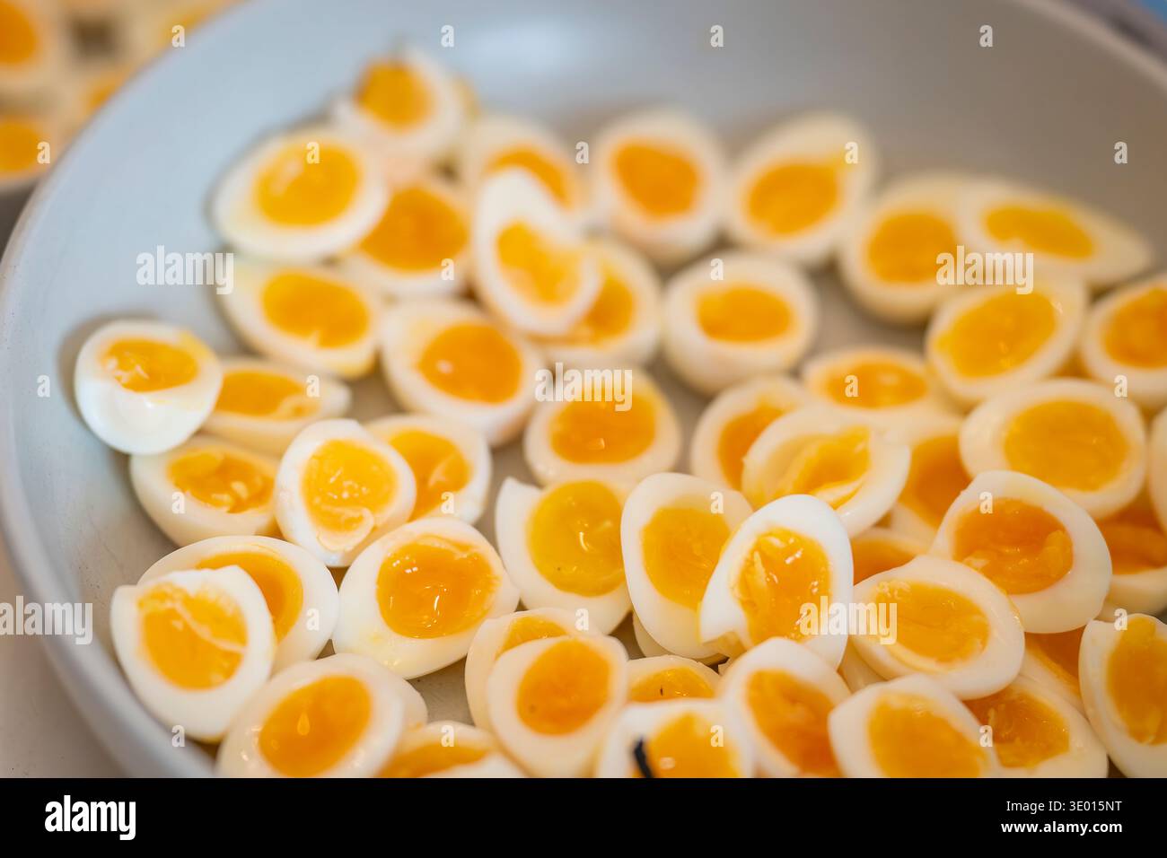 Halved soft-boiled quail eggs arranged in a white bowl, showing bright yellow yolks and delicate egg whites. Close-up of sliced quail eggs. Stock Photo