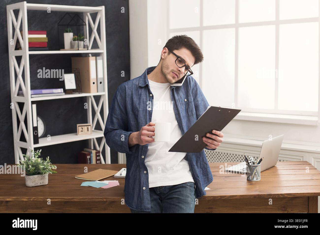Pensive young businessman talking on mobile and reading documents Stock Photo