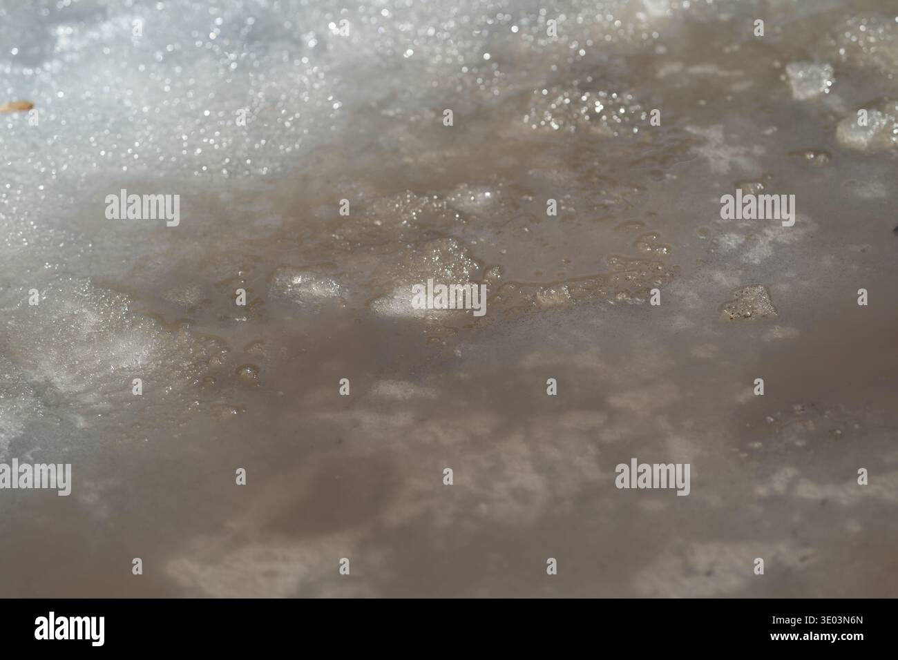 Gritty slush with spring stream closeup, coarse particles and wet sheen ...