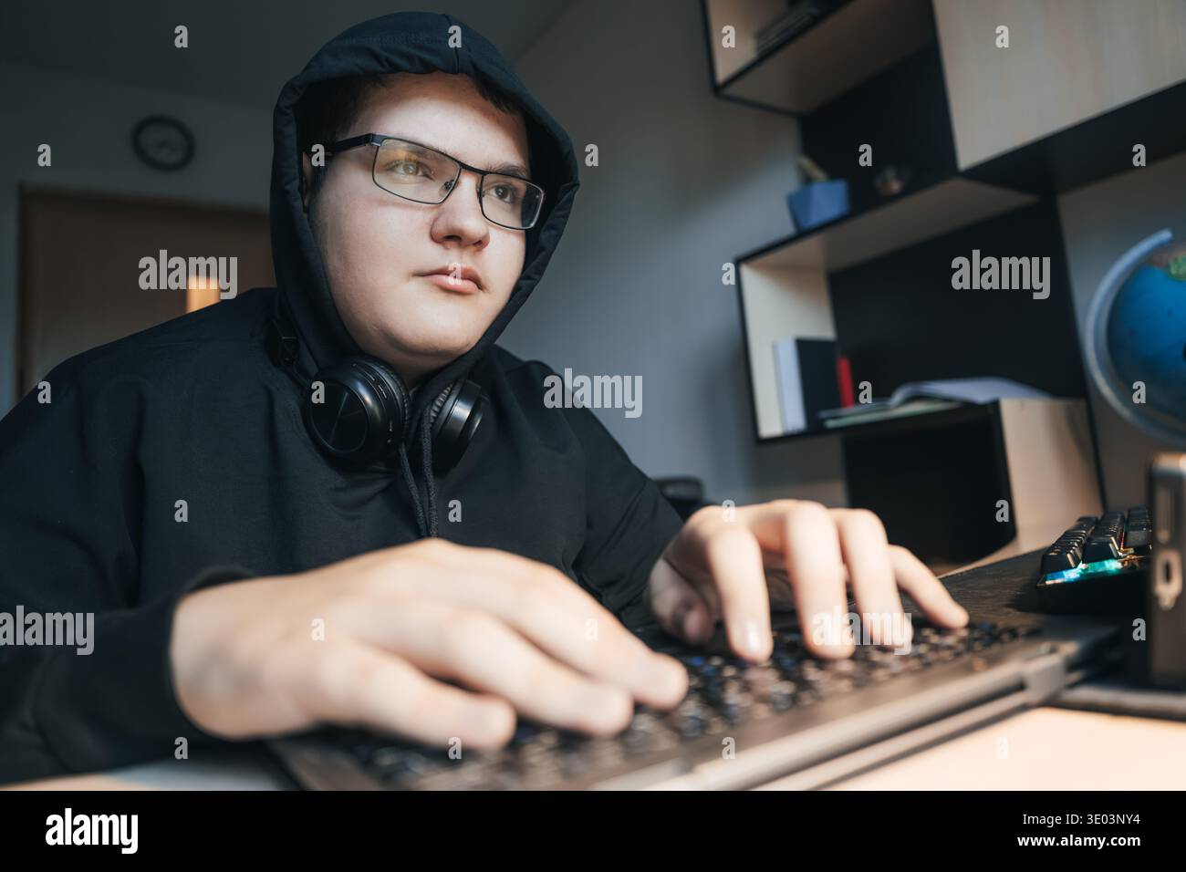 A teenage hacker or programmer works intently at his computer, typing code in a dark room. Stock Photo