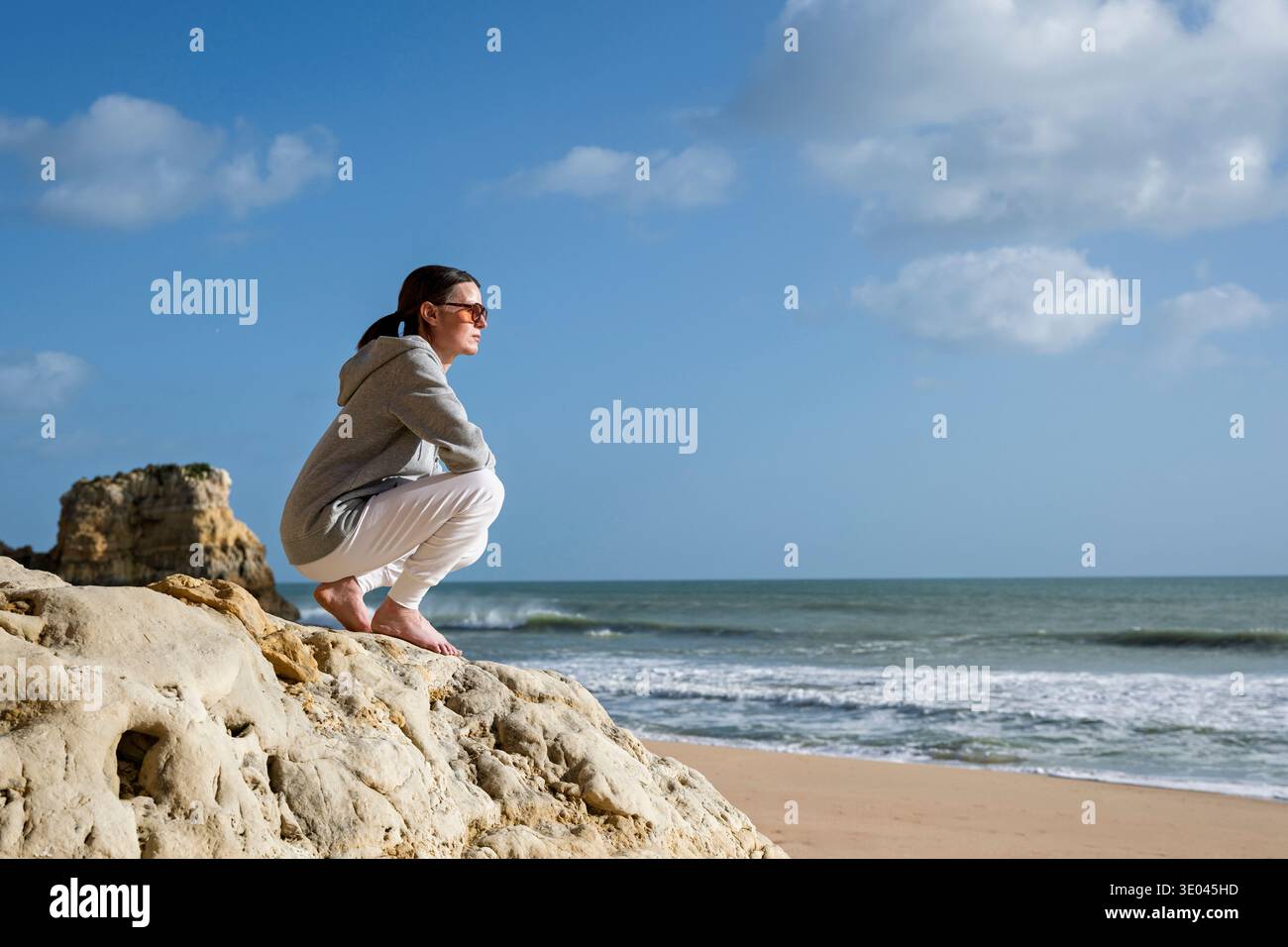 sporty woman sitting on rocks by the sea looking at the view Stock Photo