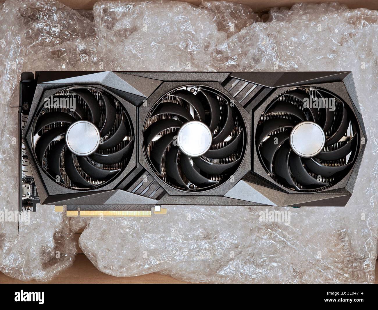 Brand new triple fan graphics card resting in bubble wrap inside an open shipping box, top view of modern high end GPU hardware protected for delivery Stock Photo